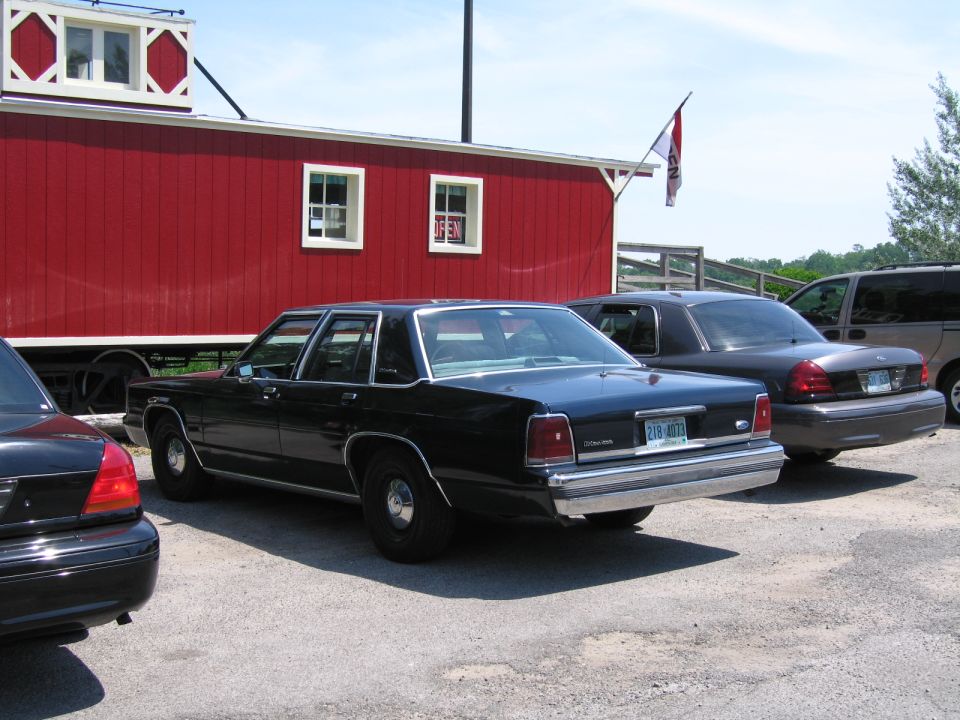 Black 2001 Ford Crown Victoria parked next to a red building