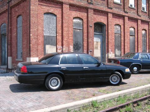 2001 Ford Crown Victoria - Photograph of a black Ford Crown Victoria by a brick building, not a technical document.