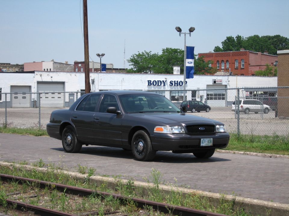 Gray Ford Crown Victoria parked on brick pavement near a body shop