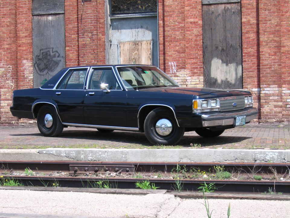 Dark Ford LTD Crown Victoria sedan parked on brick by an old building