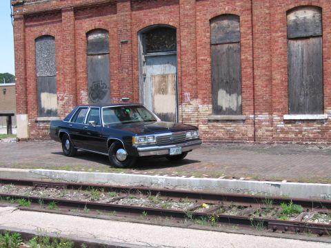 2001 Ford Crown Victoria - Photo of a dark blue Ford LTD Crown Victoria sedan parked near railroad tracks in front of a derelict brick building.