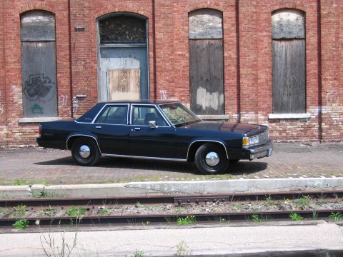 2001 Ford Crown Victoria - Photo of a dark blue Ford LTD Crown Victoria sedan parked in front of a weathered brick building.