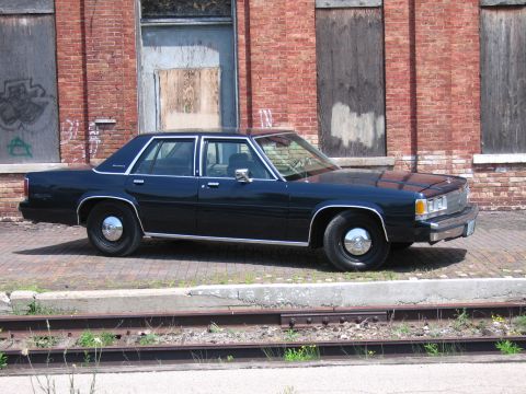 2001 Ford Crown Victoria - Photo of a dark blue Ford LTD Crown Victoria sedan parked beside an old brick wall and rail tracks.