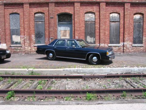 2001 Ford Crown Victoria - Photo of a dark blue Ford LTD Crown Victoria sedan parked along railroad tracks by a brick building.