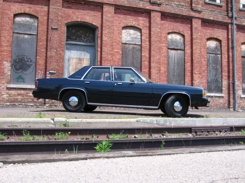 2001 Ford Crown Victoria - Photo of a dark blue Ford LTD Crown Victoria sedan parked beside railroad tracks at a brick warehouse.