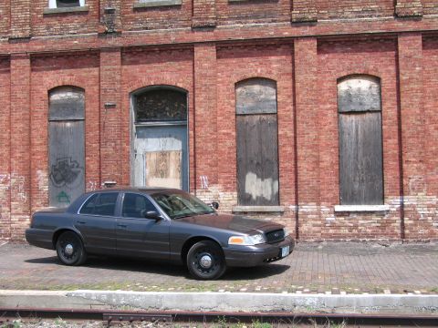 2001 Ford Crown Victoria - Photo of a gray Ford Crown Victoria sedan parked beside railroad tracks at an old brick building.