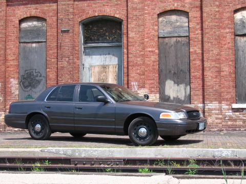 2001 Ford Crown Victoria - Photo of a gray Ford Crown Victoria sedan parked in front of a weathered brick building.