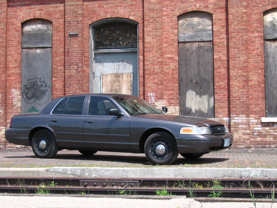 Front three-quarter view of a gray Ford Crown Victoria sedan by a brick wall