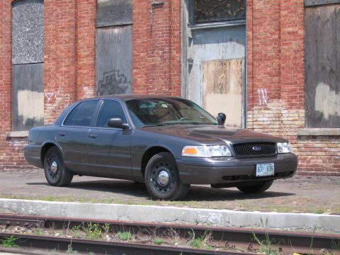 2001 Ford Crown Victoria - Photo of a gray Ford Crown Victoria sedan parked beside railroad tracks at a brick building.