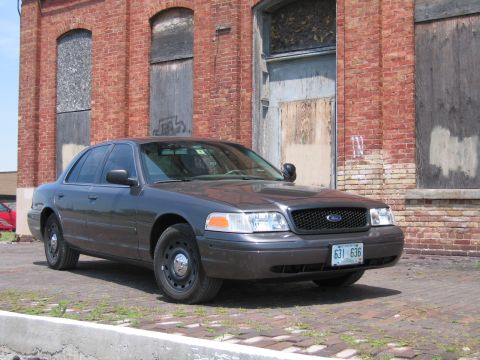 2001 Ford Crown Victoria - Photo of a gray Ford Crown Victoria sedan parked in front of a weathered brick building.