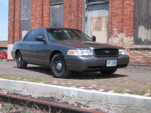 2001 Ford Crown Victoria - Photo of a gray Ford Crown Victoria sedan parked near railroad tracks at an old brick building.