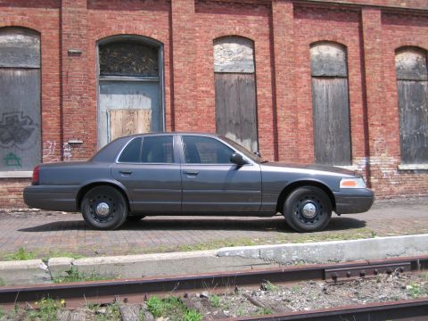 2001 Ford Crown Victoria - Photo of a gray Ford Crown Victoria sedan parked beside railroad tracks at a brick building.