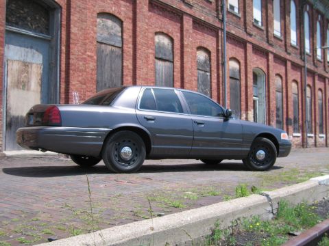 2001 Ford Crown Victoria - Photo of a gray Ford Crown Victoria sedan parked on brick pavement near a long brick warehouse.