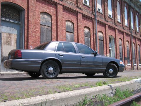 2001 Ford Crown Victoria - Photo of a gray Ford Crown Victoria sedan parked along railroad tracks at a brick building.