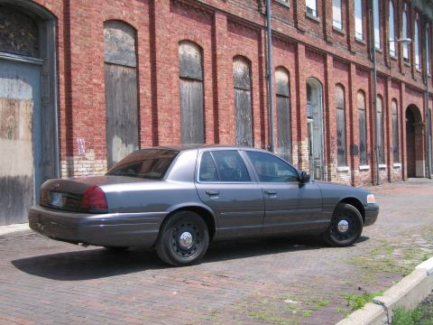 2001 Ford Crown Victoria - Photo of a gray Ford Crown Victoria sedan parked in front of a long brick warehouse.