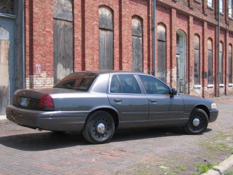 2001 Ford Crown Victoria - Photo of a gray Ford Crown Victoria sedan parked on brick pavement near a brick warehouse.