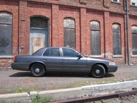 2001 Ford Crown Victoria - Photo of a gray Ford Crown Victoria sedan parked beside railroad tracks at a brick building.