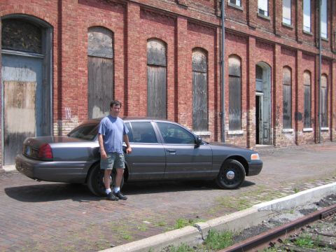 2001 Ford Crown Victoria - Photo of a man standing next to a gray Ford Crown Victoria sedan parked at a brick warehouse.