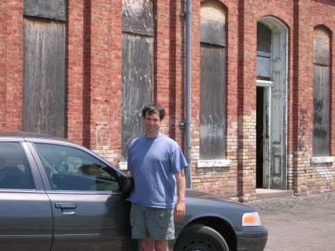2001 Ford Crown Victoria - Photo of a man standing next to a gray Ford Crown Victoria sedan in front of a brick building.