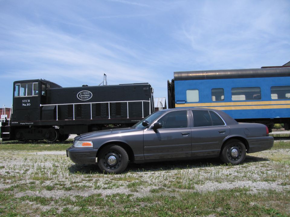 Gray Ford Crown Victoria sedan parked beside a railroad locomotive and rail car