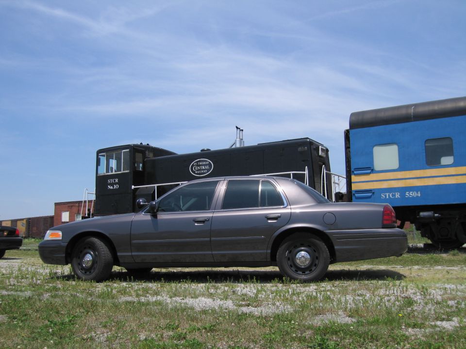 Gray Ford Crown Victoria sedan parked beside a railroad locomotive and rail car