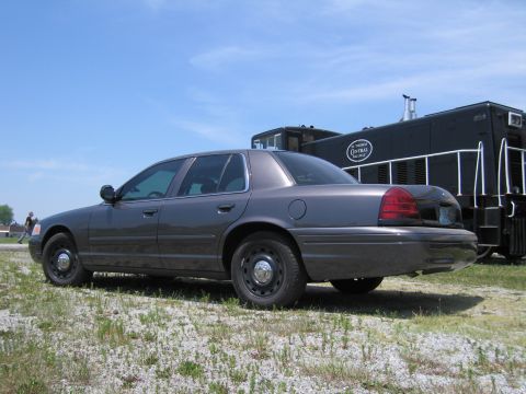 2001 Ford Crown Victoria - Photo of a gray Ford Crown Victoria sedan parked outdoors next to a black railroad caboose, not a technical document.