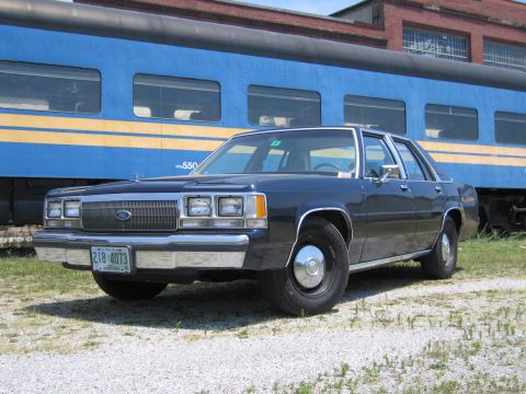 2001 Ford Crown Victoria - Photo of a black Ford LTD Crown Victoria sedan posed in front of a blue and yellow passenger train car.