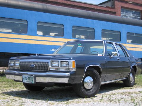 2001 Ford Crown Victoria - Photo of a black Ford LTD Crown Victoria sedan parked beside a blue and yellow passenger train car.