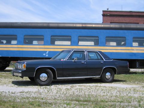 2001 Ford Crown Victoria - Side-profile photo of a black Ford Crown Victoria sedan parked beside a blue passenger train car.