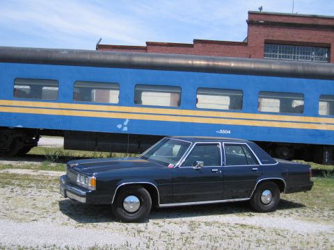 2001 Ford Crown Victoria - Photo of a black Ford Crown Victoria sedan parked beside a blue STCR 5504 passenger train car.