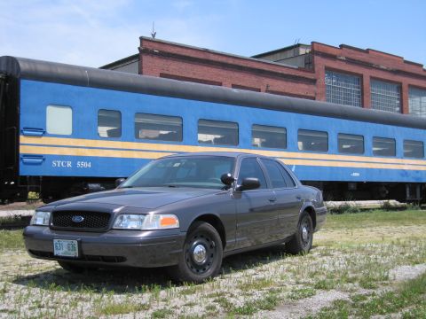 2001 Ford Crown Victoria - Photo of a gray Ford Crown Victoria sedan posed in front of a blue STCR 5504 passenger train car.