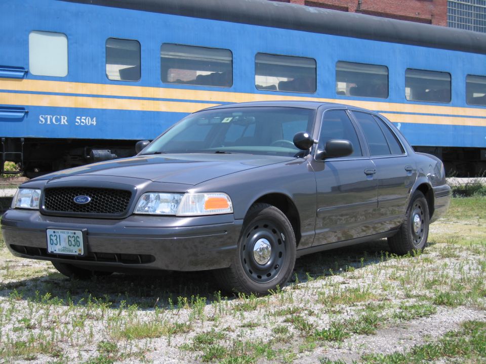 Gray Ford Crown Victoria sedan in front of a blue STCR 5504 passenger rail car