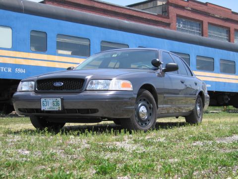 2001 Ford Crown Victoria - Photo of a gray Ford Crown Victoria sedan posed in front of a blue passenger train car.