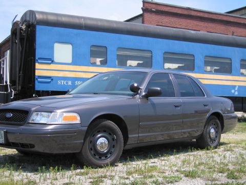 2001 Ford Crown Victoria - Side-profile photo of a gray Ford Crown Victoria sedan parked beside a blue passenger train car.