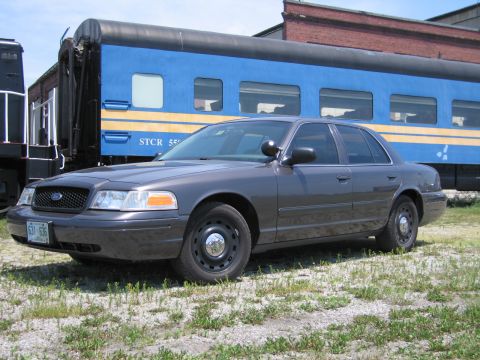 2001 Ford Crown Victoria - Photo of a gray Ford Crown Victoria sedan parked in front of a blue STCR passenger train car.