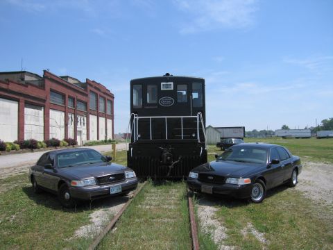 2001 Ford Crown Victoria - Photo of two Ford Crown Victoria sedans on rail tracks in front of a black railway switcher locomotive.