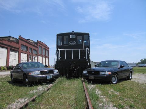 2001 Ford Crown Victoria - Photo of two Ford Crown Victoria sedans on rail tracks flanking a black railway switcher locomotive.