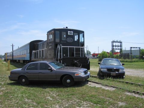2001 Ford Crown Victoria - Photo of gray and black Ford Crown Victoria sedans parked beside a black railway switcher locomotive.