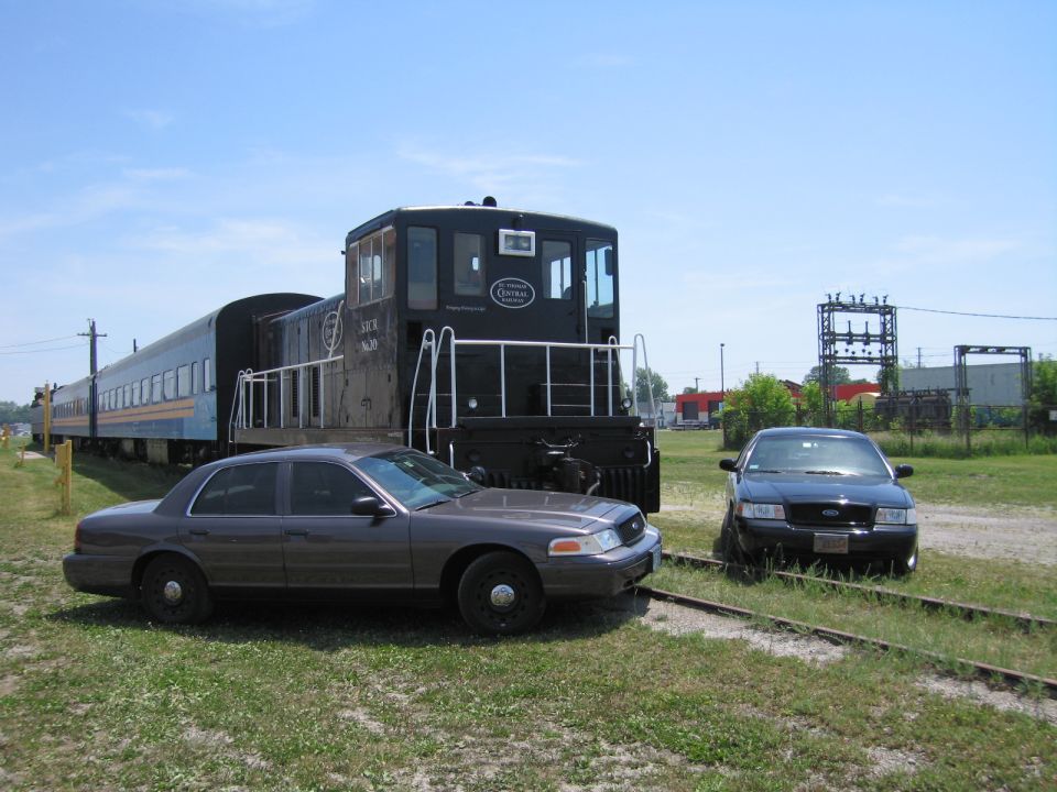Gray and black Ford Crown Victoria sedans beside a black railway switcher