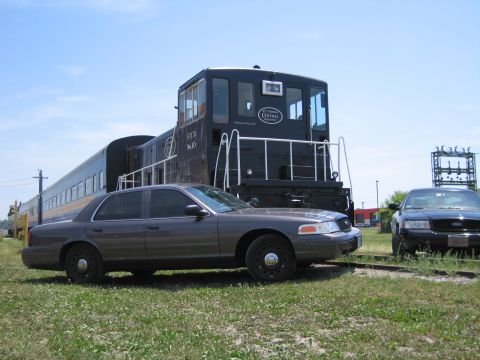 2001 Ford Crown Victoria - Side-profile photo of a gray Ford Crown Victoria sedan parked beside a black STCR railway switcher locomotive.