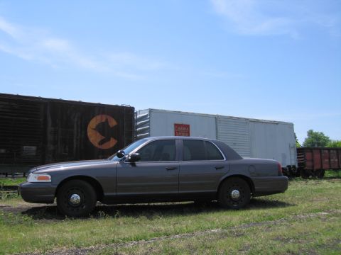 2001 Ford Crown Victoria - Photograph of a gray Ford Crown Victoria parked in front of weathered Canadian National railroad boxcars.