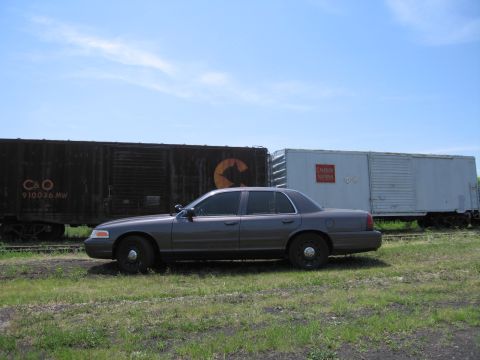 2001 Ford Crown Victoria - Photograph of a gray Ford Crown Victoria parked alongside C&O and Canadian National railroad boxcars.