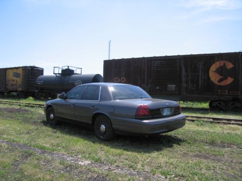 2001 Ford Crown Victoria - Photograph of a gray Ford Crown Victoria parked beside a railway tank car and a rusty C&O boxcar.