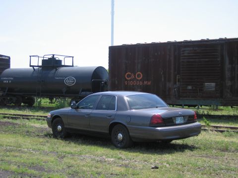 2001 Ford Crown Victoria - Photograph of a gray Ford Crown Victoria sedan between a black railway tank car and a C&O boxcar.