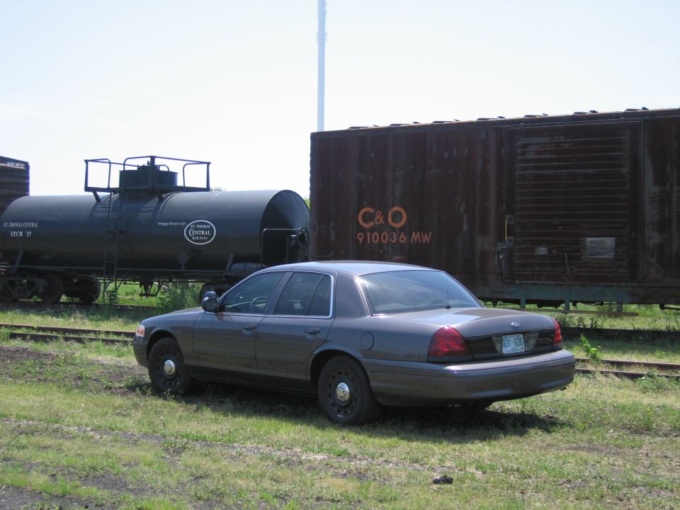 Gray Ford Crown Victoria parked between a tank car and a C&O boxcar