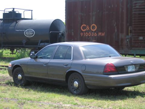 2001 Ford Crown Victoria - Photograph of a gray Ford Crown Victoria parked near a railway tank car and a rusty C&O boxcar.