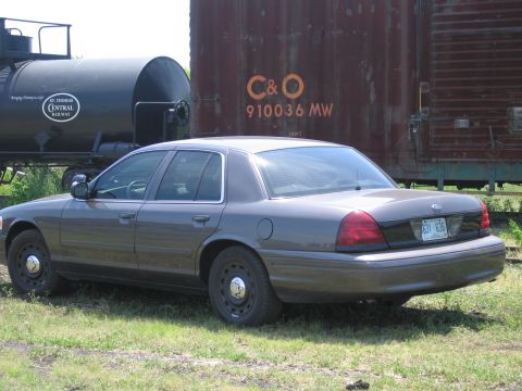 2001 Ford Crown Victoria - Photograph of a gray Ford Crown Victoria parked next to a rusty C&O railroad boxcar.