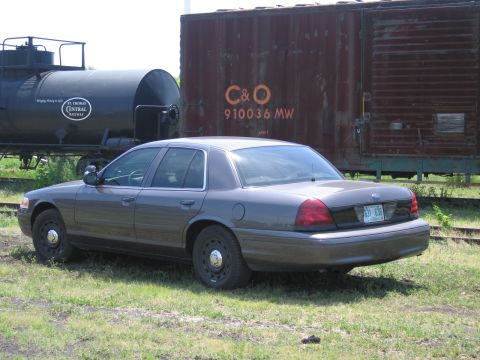 2001 Ford Crown Victoria - Photograph of a gray Ford Crown Victoria parked alongside a railway tank car and a rusty C&O boxcar.