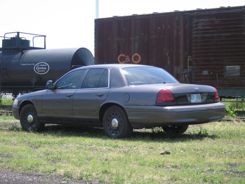 2001 Ford Crown Victoria - Photograph of a gray Ford Crown Victoria parked beside railway rolling stock in a railyard.