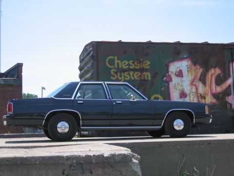 2001 Ford Crown Victoria - Photograph of a black Ford LTD Crown Victoria parked beside a graffiti-covered Chessie System boxcar.
